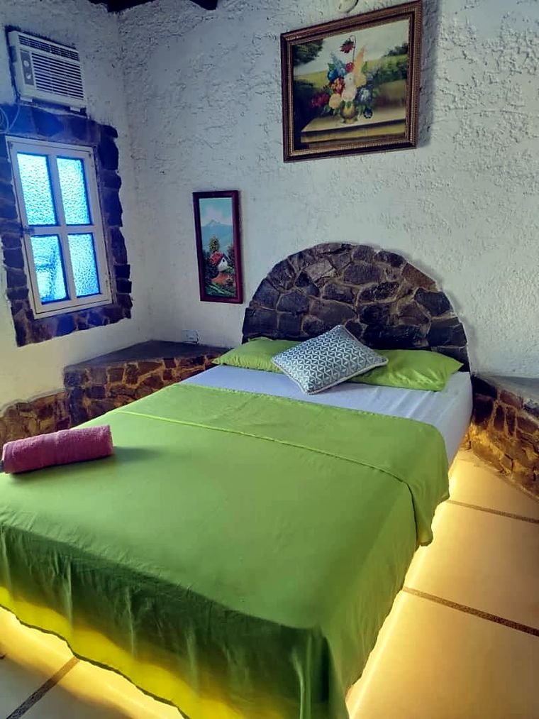 Habitación con cabecero de piedra, sábanas verdes y luz cálida
