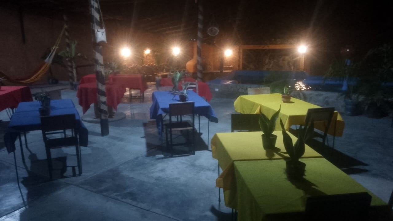 Terraza techada de noche con mesas de colores y luces